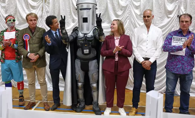 Count Binface, center, stands among other candidates during the result announcement after the Clacton by-election count at the Leisure Centre in Clacton on Sea, England, Friday, Aug. 14, 2026.(AP Photo/Richard Pelham)