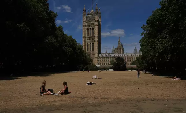 People sit on dried grass in a park outside the Houses of Parliament in London, Monday, Aug. 10, 2026. (AP Photo/Kin Cheung)