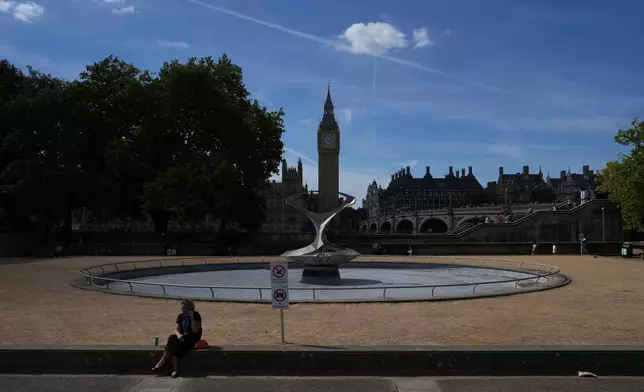 A woman sits in front of the Houses of Parliament in London, Monday, Aug. 10, 2026. (AP Photo/Kin Cheung)