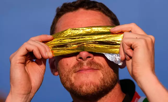 A spectator watches the solar eclipse at the European Athletics Championships in Birmingham, England, Wednesday, Aug. 12, 2026. (AP Photo/Petr David Josek)