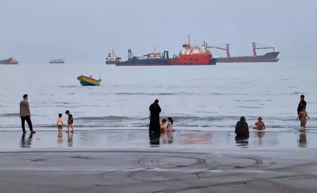 People spend time at a beach as commercial vessels are anchored in the Strait of Hormuz off Bandar Abbas, Iran, Wednesday, Aug. 5, 2026. (Amirhosein Khorgooi/ISNA via AP)
