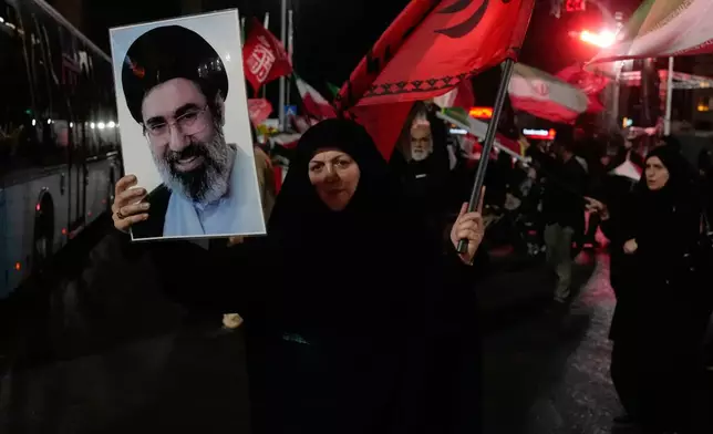 A woman holds up a poster of Iranian Supreme Leader Ayatollah Mojtaba Khamenei and waves a flag during a pro-government gathering at a square in Tehran, Iran, Tuesday, Aug. 11, 2026. (AP Photo/Vahid Salemi)