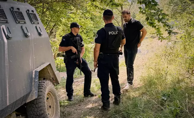 Erblin Ademi, right, whose father, Adem Ademi, a prominent surgeon, disappeared along with 22 other intellectuals during the Kosovo war in April 1999, speaks to police officers near the excavation site of a mass grave in Small Kalluder, Kosovo, Wednesday, Aug. 5, 2026. (AP Photo/Zana Cimili)