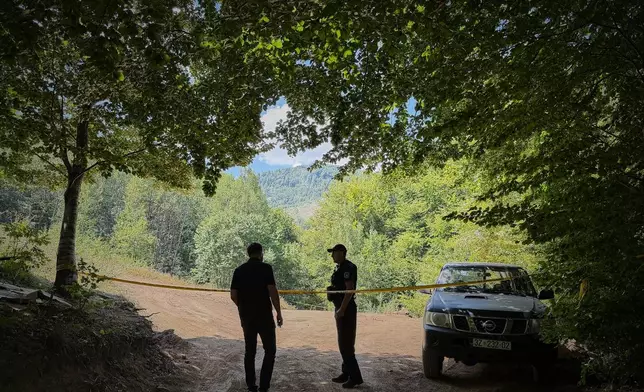 Erblin Ademi, left, whose father, Adem Ademi, a prominent surgeon, disappeared along with 22 other intellectuals during the Kosovo war in April 1999, speaks to a police officer near the excavation site of a mass grave in Small Kalluder, Kosovo, Wednesday, Aug. 5, 2026. (AP Photo/Zana Cimili)
