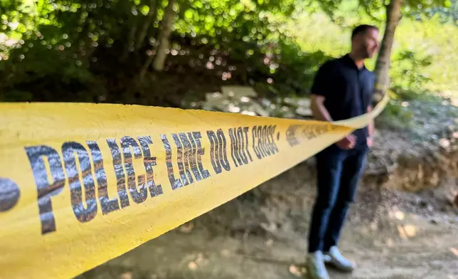 Erblin Ademi, right, whose father, Adem Ademi, a prominent surgeon, disappeared along with 22 other intellectuals during the Kosovo war in April 1999, stands behind yellow police tape near the excavation site of a mass grave in Small Kalluder, Kosovo, Wednesday, Aug. 5, 2026. (AP Photo/Zana Cimili)