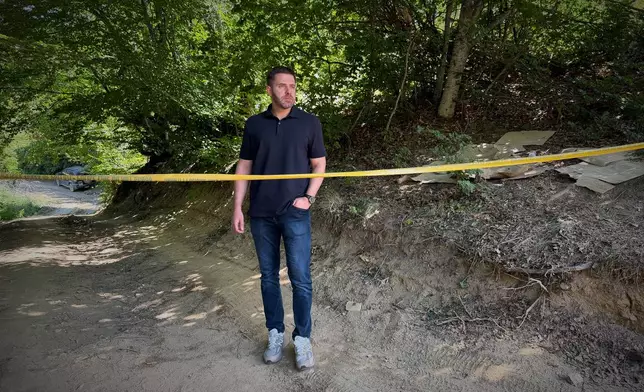Erblin Ademi, whose father, Adem Ademi, a prominent surgeon, disappeared along with 22 other intellectuals during the Kosovo war in April 1999, stands behind yellow tape near the excavation site of a mass grave in Small Kalluder, Kosovo, Wednesday, Aug. 5, 2026. (AP Photo/Zana Cimili)