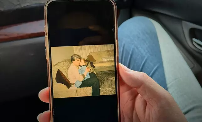 Erblin Ademi, right, whose father, Adem Ademi, a prominent surgeon, disappeared along with 22 other intellectuals during the Kosovo war in April 1999, shows a photo of him and his father, near the excavation site of a mass grave in Small Kalluder, Kosovo, Wednesday, Aug. 5, 2026. (AP Photo/Zana Cimili)