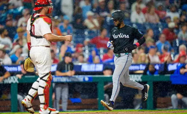 Miami Marlins' Otto Lopez, right, comes in to score on a single hit by Griffin Conine as Philadelphia Phillies catcher J.T. Realmuto, left, looks on during the sixth inning of a baseball game, Monday, Aug. 17, 2026, in Philadelphia. (AP Photo/Chris Szagola)