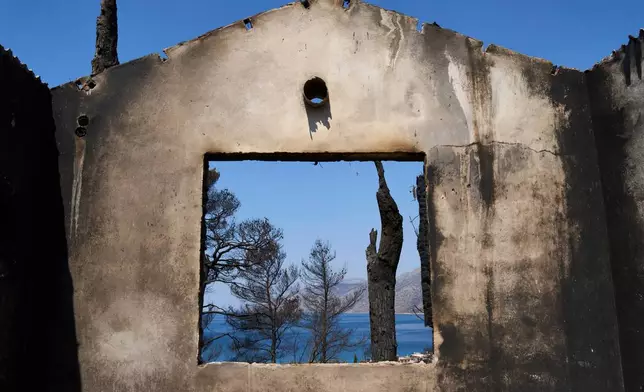 The sea is visible through the remains of a house destroyed by a wildfire in Porto Germeno, northwest of Athens, Greece, Tuesday, Aug. 4, 2026. (AP Photo/Petros Giannakouris)