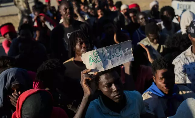 A migrant who crossed from Morocco into Spain holds a sign reading, in Spanish, "asylum" as he lines up for food distribution on a beach in the Spanish enclave of Ceuta, Monday, Aug. 3, 2026. (AP Photo/Bernat Armangue)