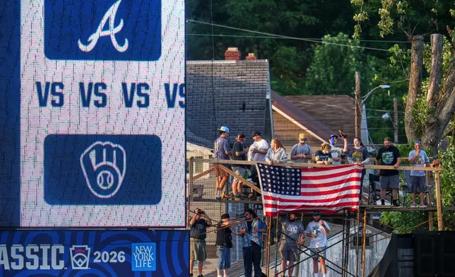 Fans on a scaffold beyond the outfield fence at Bowman Field watch the opening ceremony before the Little League Classic baseball game between the Milwaukee Brewers and the Atlanta Braves in Williamsport, Pa., Sunday, Aug. 23, 2026. (AP Photo/Gene J. Puskar)