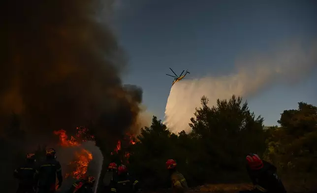A firefighting helicopter drops water over a smoke-filled forest during a wildfire near Porto Germeno, northwest of Athens, Greece, Sunday, Aug. 2, 2026. (AP Photo/Michael Varaklas)