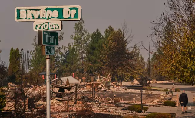 A street sign shows sign of fire damage as a person walks their dog after a wildfire hit the northern part of Spokane, Wash., Monday, Aug. 3, 2026. (AP Photo/Lindsey Wasson)