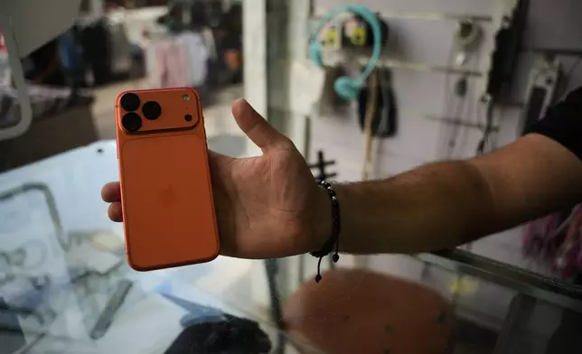 A Palestinian salesman shows an iPhone 17 Pro Max to the camera at a mobile phone store in Gaza City, Sunday, Aug. 16, 2026. (AP Photo/Abdel Kareem Hana)