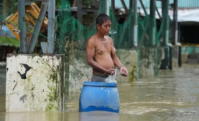 A man smokes along floodwaters caused by heavy seasonal monsoon rains at Bagong Silangan village in Quezon city, Metro Manila, Philippines, Monday, Aug. 10, 2026. (AP Photo/Aaron Favila)