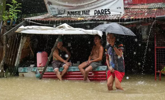 Residents stay at a store along floodwaters caused by heavy seasonal monsoon rains at Bagong Silangan village in Quezon city, Metro Manila, Philippines, Monday, Aug. 10, 2026. (AP Photo/Aaron Favila)