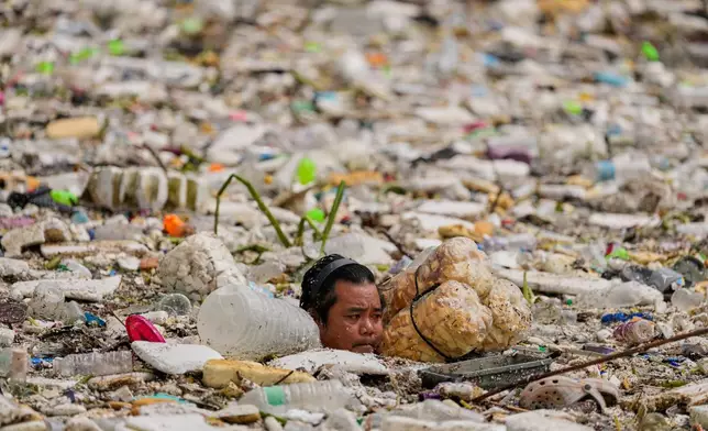 A worker uses improvised floats while trying to clear a sea of garbage and debris brought by intense monsoon rains at the Redemptorist Water Channel in Paranaque city, Metro Manila, Philippines on Tuesday, Aug. 11, 2026. (AP Photo/Aaron Favila)