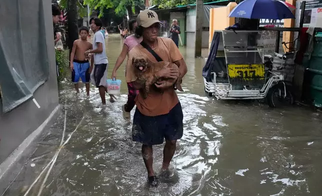 A man carries his dog along floodwaters caused by heavy seasonal monsoon rains at Bagong Silangan village in Quezon city, Metro Manila, Philippines Monday, Aug. 10, 2026. (AP Photo/Aaron Favila) CORRECTION: Corrects typo in location to Silangan, instead of Silagan