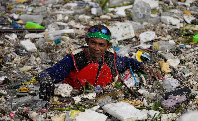 A worker tries to clear a sea of garbage and debris brought by intense monsoon rains at the Redemptorist Water Channel in Paranaque city, Metro Manila, Philippines Tuesday, Aug. 11, 2026. (AP Photo/Aaron Favila)