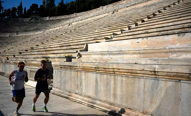 Two men run at the Panathenaic Stadium, also known as "Kallimarmaro," or beautiful marble, which hosted the first modern Olympic Games in 1896, during renovation work in Athens, Greece, Thursday, Aug. 13, 2026. (AP Photo/Thanassis Stavrakis)