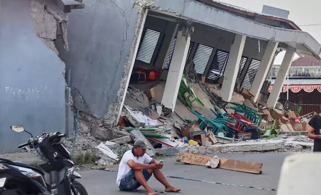 A man checks his phone near a building collapsed due to an earthquake, in Reok, East Nusa Tenggara province, Indonesia, Sunday, Aug. 16, 2026. (AP Photo/Aquila Handayani Abbas)