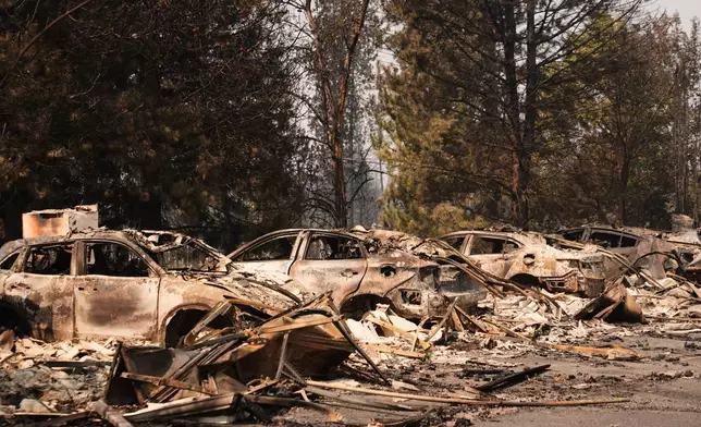 A line of burned cars sit in a parking lot Tuesday, Aug. 4, 2026, after a wildfire hit the northern part of Spokane, Wash. (AP Photo/Lindsey Wasson)