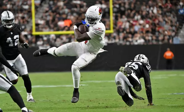 Arizona Cardinals running back Jeremiyah Love, center, spins away from Las Vegas Raiders cornerback Hezekiah Masses during the first half of a preseason NFL football game, Thursday, Aug. 13, 2026, in Las Vegas. (AP Photo/David Becker)
