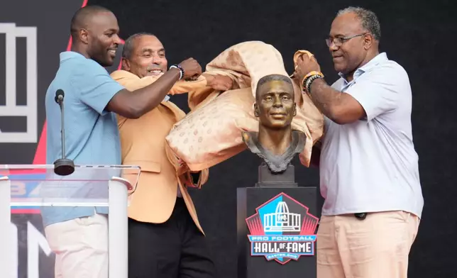 Former NFL player Roger Craig, center, unveils his bust with son, Roderick Craig, left, and Jamie Williams during the Pro Football Hall of Fame induction ceremony at the Pro Football Hall of Fame, in Canton, Ohio, Saturday, Aug. 8, 2026. (AP Photo/Sue Ogrocki)