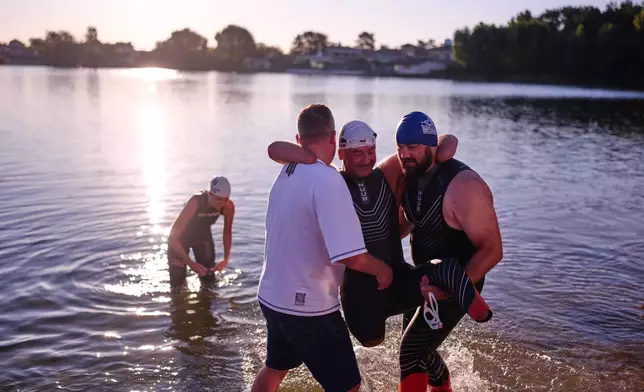 Ukrainian war veteran Oleksii Kozak is helped to get out of the water during a sporting event to encourage people and injured soldiers to take part in sports at a lake on the outskirts of Kyiv, Monday, Aug. 24, 2026, during the 35th anniversary of Ukraine's Independence Day. (AP Photo/Francisco Seco)