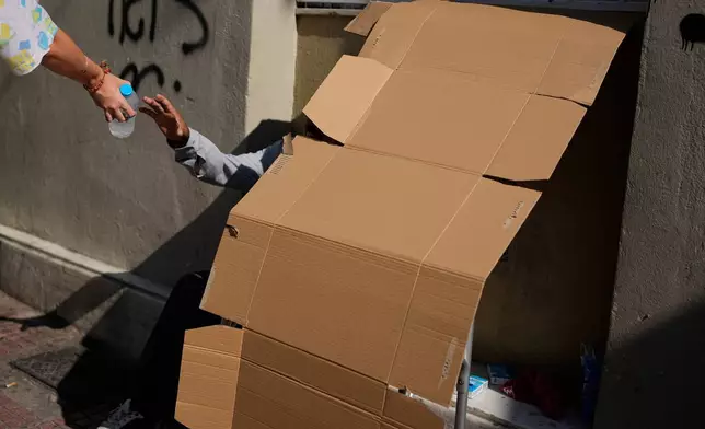 A homeless Syrian refugee receives cold water from the Streetwork team of the Athens municipality's Department of Social Solidarity during a heat wave in Athens, Greece, Monday, Aug. 24, 2026. (AP Photo/Thanassis Stavrakis)