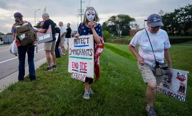 A masked protester walks with a sign during an "ICE out of Cincinnati" protest across the street from the ICE Enforcement and Removal Operations field office as Haitians who reside in Ohio arrive for appointments in Cincinnati, Sunday, Aug. 2, 2026. (AP Photo/Carolyn Kaster)