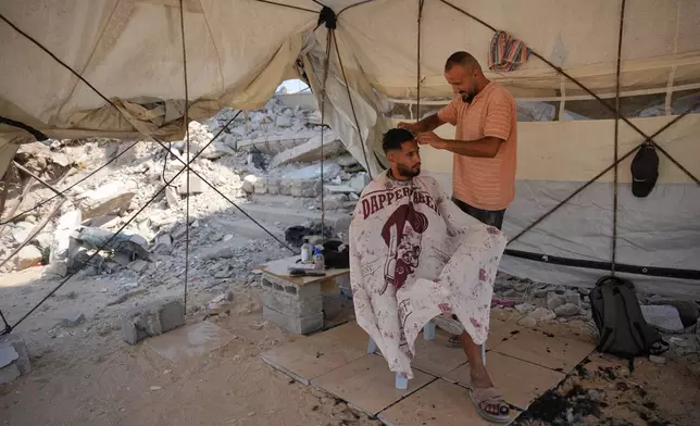 Palestinian barber Mousa al-Kharibi gives a man a haircut inside a tent, by the rubble of buildings that were destroyed during the Israel Hamas war, in Khan Younis, southern Gaza Strip, Friday, July 31, 2026. (AP Photo/Abdel Kareem Hana)