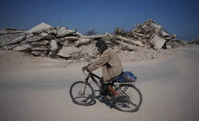A Palestinian man rides his bicycle by the rubble of buildings that were destroyed during the Israel Hamas war, in Khan Younis, southern Gaza Strip, Friday, July 31, 2026. (AP Photo/Abdel Kareem Hana)
