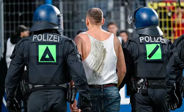 An SV Waldhof Mannheim supporter is escorted away off the pitch by police officers during the Germany Cup soccer match between SV Waldhof Mannheim and 1. FC Kaiserslautern, Friday, Aug. 21, 2026, in Mannheim, Germany. (Uwe Anspach/dpa via AP)