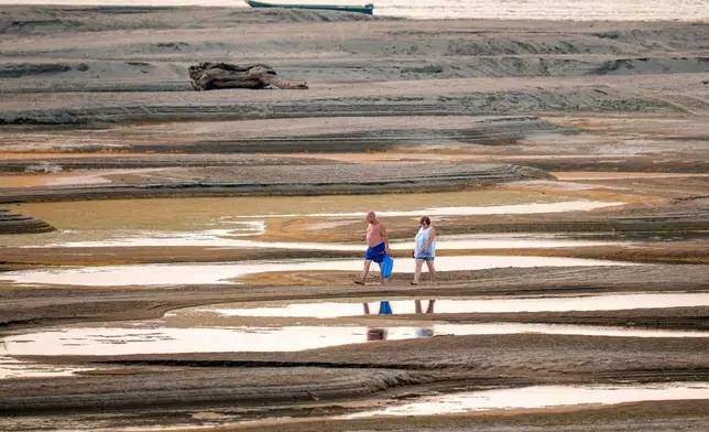 People walk on a sandbank on the Danube River as usually submerged areas are exposed amid exceptionally low water levels, in Rasova, Romania, Friday, Aug. 7, 2026. (AP Photo/Andreea Alexandru)