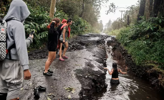 A teenager wades through a pool of water in a washed-out section of a damaged road in Mountain View, Hawaii, Sunday, Aug. 16, 2026, after a severe weather system went through the area. (Stephen Lam/San Francisco Chronicle via AP)