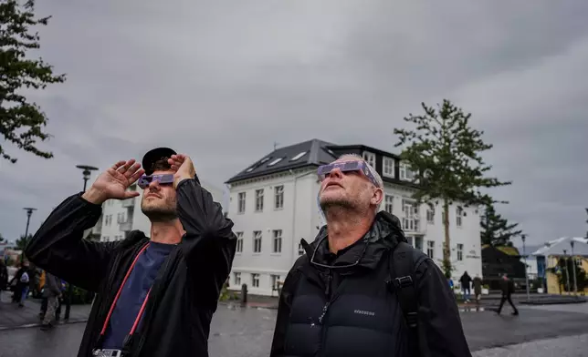 People use solar eclipse glasses to look up at the sun ahead of a solar eclipse Reykjavik, Iceland, Wednesday, Aug. 12, 2026. (AP Photo/Marco di Marco)