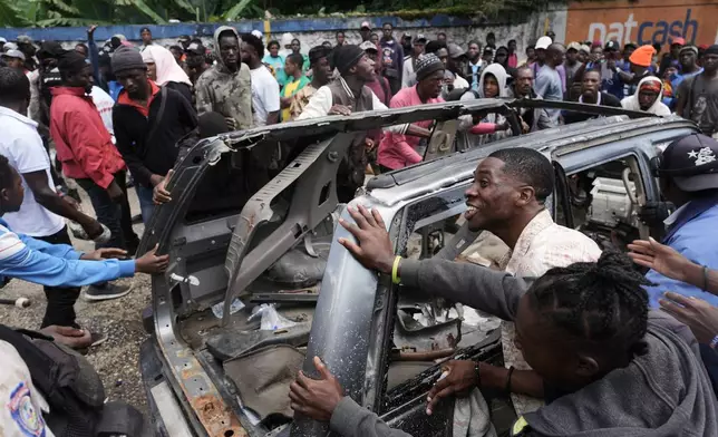 Residents try to flip over a car to block a street as they protest for police intervention after deadly gang attacks in the Kenscoff neighborhood of Port-au-Prince, Haiti, Monday, Aug. 24, 2026. (AP Photo/Odelyn Joseph)