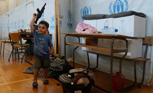 A displaced boy holds his toy rifle outside his makeshift room on a basketball court inside a public school turned into a shelter for people whose villages in southern Lebanon were destroyed or occupied by Israeli forces, in Tyre, southern Lebanon, Thursday, Aug. 27, 2026. (AP Photo/Hussein Malla)