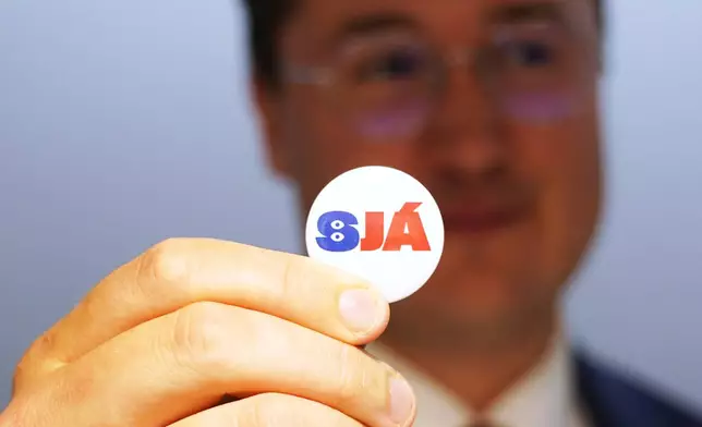 A man holds a badge reading "See", at the opening of the "Yes" campaign's office in Reykjavik, Iceland, Friday, Aug. 7, 2026. (AP Photo/James Brooks)