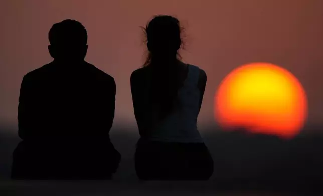 People watch the setting sun at the end of a hot summer day, Sunday, July 26, 2026, in Kansas City, Mo. (AP Photo/Charlie Riedel)