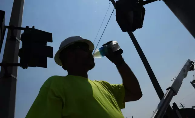 FILE - Dean Malcom drinks water while wiring street lights in extremely hot weather July 14, 2026, in Detroit. (AP Photo/Paul Sancya, File)