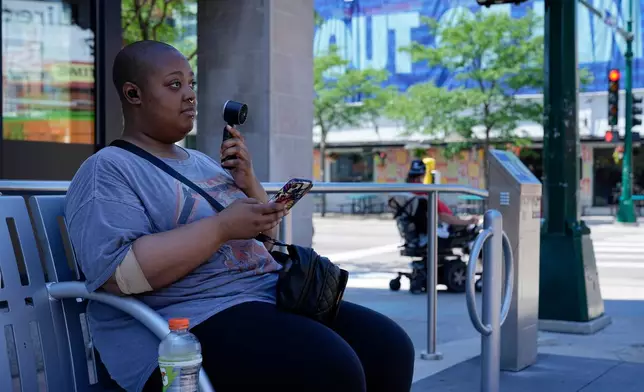 FILE - Simone Mosley waits for their ride in shade at a bus stop during an extreme heat warning July 13, 2026, in Minneapolis. (AP Photo/Ellen Schmidt, File)