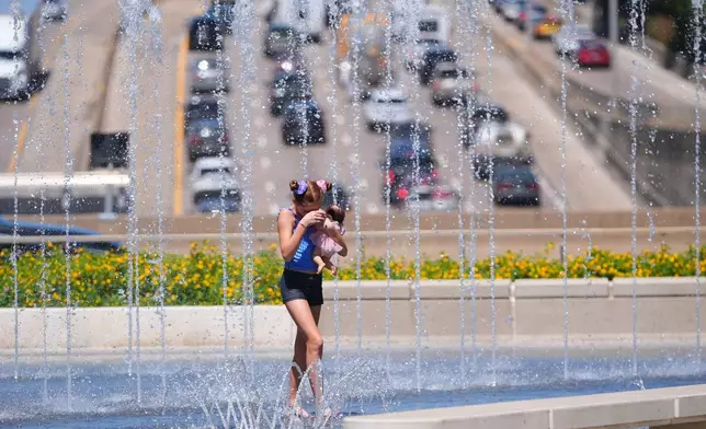 Madison Hermes, 11, carries a doll as she cools off with water fountains on a hot summer day in downtown Dallas, Monday, July 27, 2026. (AP Photo/LM Otero)