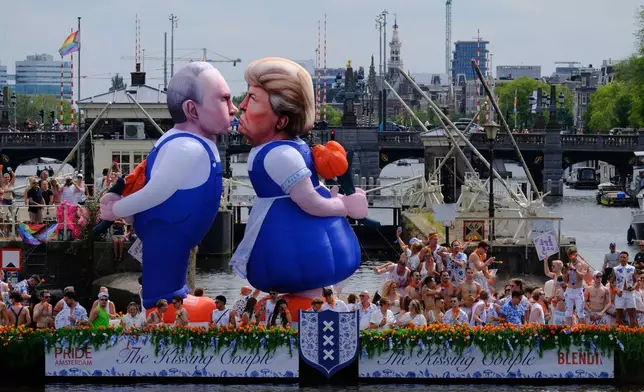 Two inflatable caricature balloons depicting U.S. President Donald Trump, center, and Russian President Vladimir Putin, left, as people line the Dutch capital's historic canals Saturday, Aug. 1, 2026, to watch the Amsterdam Pride Canal Parade. (AP Photo/Patrick Post)