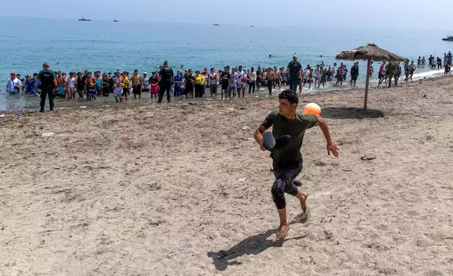 A migrant runs from Spanish police officers as they cordon off access to the beach for people crossing from Morocco into the Spanish enclave of Ceuta, Friday, July 31, 2026. (AP Photo/Antonio Sempere)