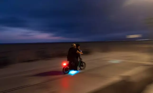 An adult rides an e-bike with a child in Santa Monica, Calif., Monday, Aug. 10, 2026. (AP Photo/Jae C. Hong)