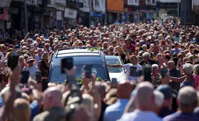 Fans of singer Bonnie Tyler line the streets as her coffin is transported in a hearse back to her former home ahead of her funeral, in Mumbles, Wales, Saturday, Aug. 15, 2026. The Total Eclipse Of The Heart musician, whose real name was Gaynor Hopkins, died in hospital in Portugal on July 8 at the age of 75. (AP Photo/Alastair Grant)