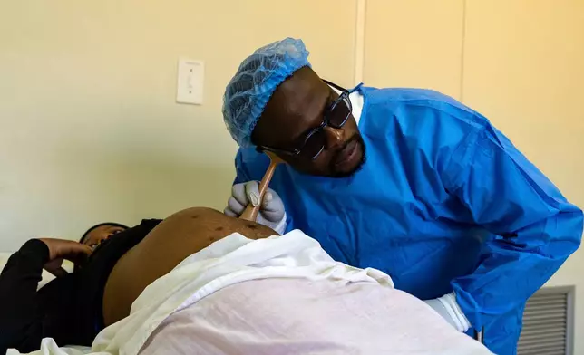 Male midwife Sehloho Ntlhane leans over a pregnant patient while using a Pinard horn to listen to the baby's heartbeat during a prenatal examination at Mpharane Health Centre in Mohale's Hoek district, Lesotho, Friday, July 10, 2026. (AP Photo/Kayleen Morgan)
