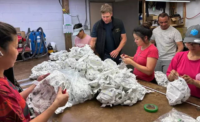 Wuxly CEO James Yurichuk and garment factory owner Aaron Lyand inspect military helmet covers on July 20, 2026, in North York, Ontario. (AP Photo/Kelvin Chan)